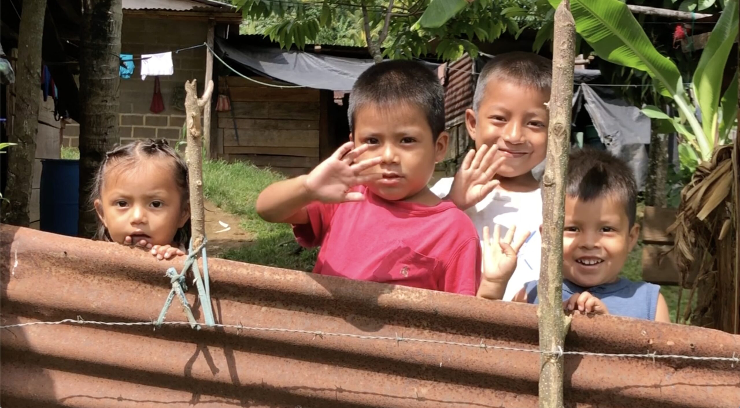 Children in Chesake, Guatemala, smiling and waving after receiving food supplies funded by Hess Construction.